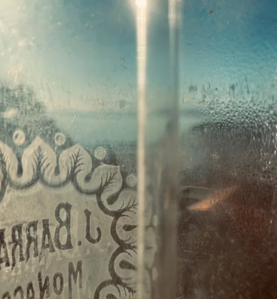 Gros plan d'un flacon en verre gravé couvert de condensation, laissant deviner une lumière bleutée en arrière-plan.